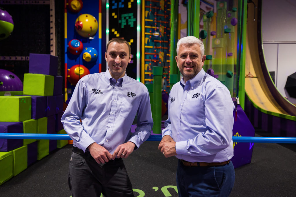 Two men in shirts stand smiling in a Clip 'n Climb centre